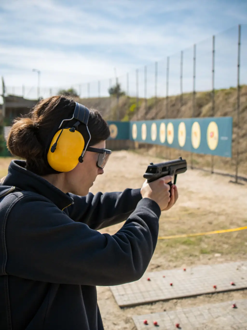 A portrait photo of a focused young adult practicing target shooting at an indoor range, wearing protective gear and aiming with concentration, representing personal growth through sport.